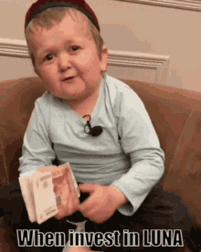 a little boy is sitting on a couch holding a stack of money with the words when invest in luna below him