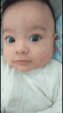 a baby in a white outfit looks at the camera