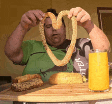 a man holding a pretzel in the shape of a heart with a glass of orange juice next to him