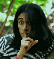 a man with long black hair is holding his finger to his mouth