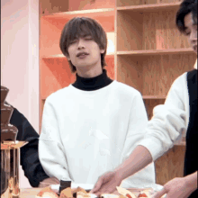 a man in a white sweater is standing in front of a table with a plate of food on it