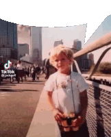 a young boy is standing on a bridge holding a binoculars in front of a city skyline .