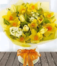 a bouquet of yellow flowers is sitting on a wooden table with a bow .