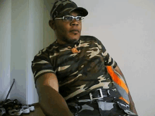 a man wearing a camouflage shirt and glasses is sitting on a chair