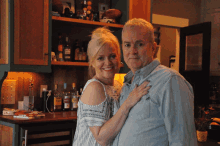 a man and a woman are posing for a picture in front of a shelf with bottles of alcohol on it