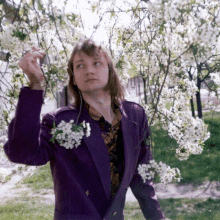 a man in a purple jacket is standing in front of a tree with white flowers on it