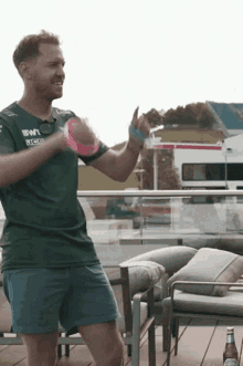 a man in a green shirt and blue shorts is dancing on a balcony with a bottle of beer .