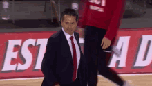 a man in a suit and tie walks on a basketball court in front of a sign that says estado