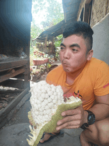 a man wearing an orange shirt that says ' abercrombie & fitch ' on it is eating a large fruit