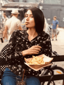 a woman sitting on a bench eating french fries and a drink