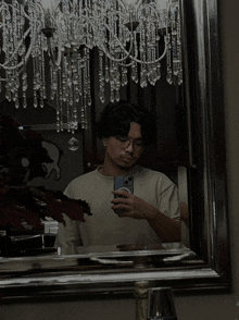 a man taking a selfie in front of a mirror with a chandelier behind him