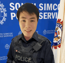 a man in a police uniform stands in front of a south simcoe police sign