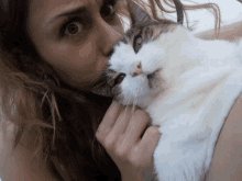 a woman kisses a cat on the nose while it looks at the camera