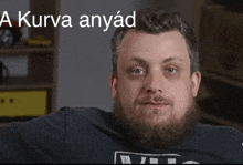 a man with a beard is sitting in front of a sign that says a kurve anyad