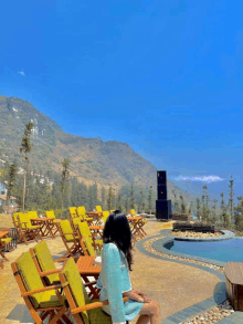 a woman sits in a chair in front of a swimming pool with mountains in the background