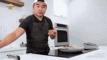 a man in an apron is standing in a kitchen with a plate of food in front of him .