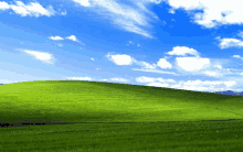 a grassy hill with a blue sky and white clouds in the background