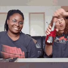 a woman holding a bottle of coca cola next to another woman wearing a shirt that says ' a ' on it