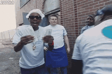 a group of men are standing in front of a brick building and one of them is wearing a chef 's hat