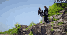 two women standing on top of a rocky hillside with a blue banner above them that says ' sbs '