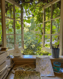 a painting sits on a table in front of an open window surrounded by greenery