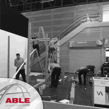 a black and white photo of a group of men working on a building with able written on the bottom