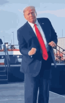 donald trump is dancing on a stage while wearing a suit and red tie .