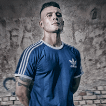 a man in a blue adidas shirt stands with his arms crossed