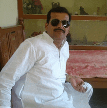 a man wearing sunglasses and a white shirt is sitting on a bed