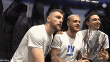 three men are posing for a picture in a locker room with one wearing a shirt that says 7m winner