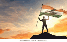 a man is holding an indian flag on top of a mountain at sunset .