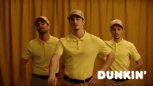 three men wearing yellow dunkin ' shirts and hats stand in front of a yellow curtain