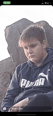 a young man wearing a blue puma hoodie sits in front of a large rock