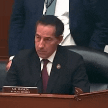 a man in a suit and tie is sitting at a desk with a name plate that says mr. baskin .