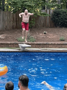 a man is jumping into a swimming pool with a fence in the background