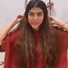 a woman with long hair is wearing a red shirt and holding her hair in front of a clock .