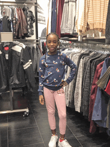 a little girl wearing a blue sweater and pink sweatpants stands in a clothing store