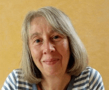 a woman with gray hair is wearing a striped shirt and smiling for the camera .