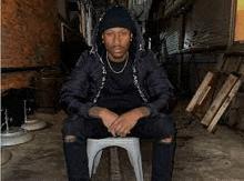 a man in a black jacket is sitting on a white stool in a dark alleyway .