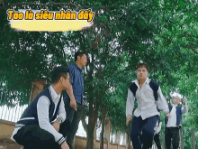 a group of young men are standing in front of trees with a yellow sign that says tao la siêu nhân day