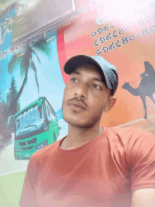 a man wearing a hat and a red shirt stands in front of a poster with a green bus and a camel on it