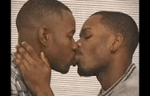 two black men are kissing each other in front of a window .