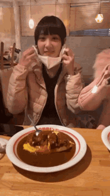 a woman wearing a face mask sits at a table with a plate of food that says curry on it