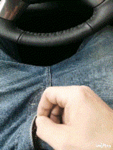 a close up of a person 's hand on a pair of jeans with a steering wheel in the background