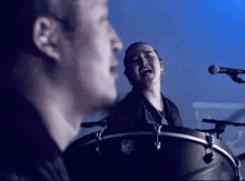 a man singing into a microphone next to a man playing a drum