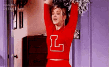 a cheerleader wearing a red sweater with the letter l on it is holding pom poms in her hands .