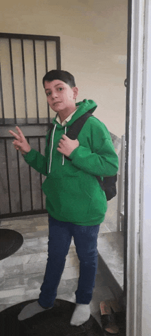 a young boy wearing a green hoodie and a black backpack stands in front of a door