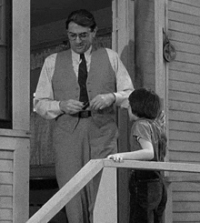 a man in a vest and tie is standing on a porch with a boy .