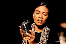 a woman is singing into a microphone while wearing a pearl necklace .