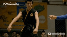 a man in a karate uniform is standing in front of a crowd of people in a gym .